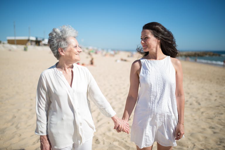Madre e Hija caminando por la playa. Madre adulta vestida de blanco, hija adulta vestida de blanco.